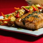 Pan-seared salmon fillet drizzled with garlic butter, garnished with fresh parsley and lemon slices, served on a white plate