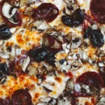 A close-up image of a freshly baked pizza with a variety of toppings, including, olives, and sliced beets.