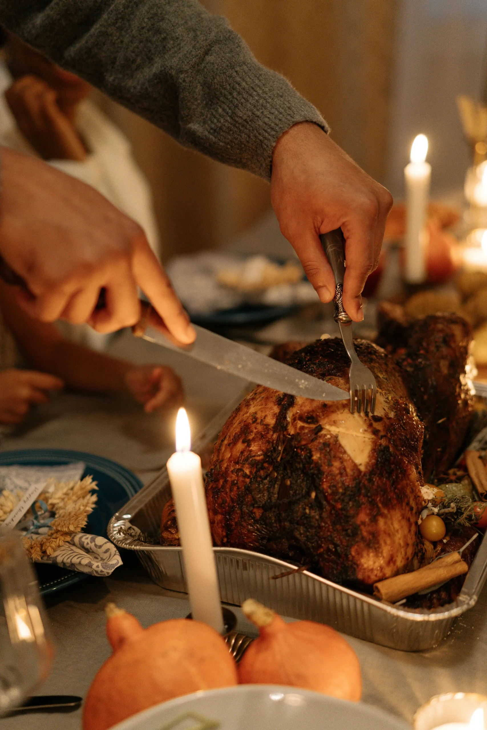 Close-up of hands carving a perfectly smoked turkey with a golden-brown crust, served on a festive Thanksgiving table surrounded by candles and pumpkins