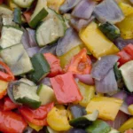 Close-up of colorful roasted vegetable medley with red peppers, yellow squash, zucchini, and red onions, glistening with olive oil and seasoning