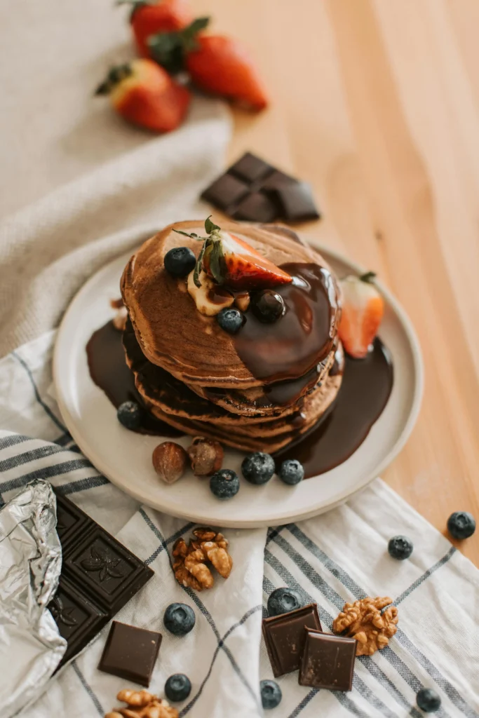 A stack of chocolate chip pancakes drizzled with chocolate syrup