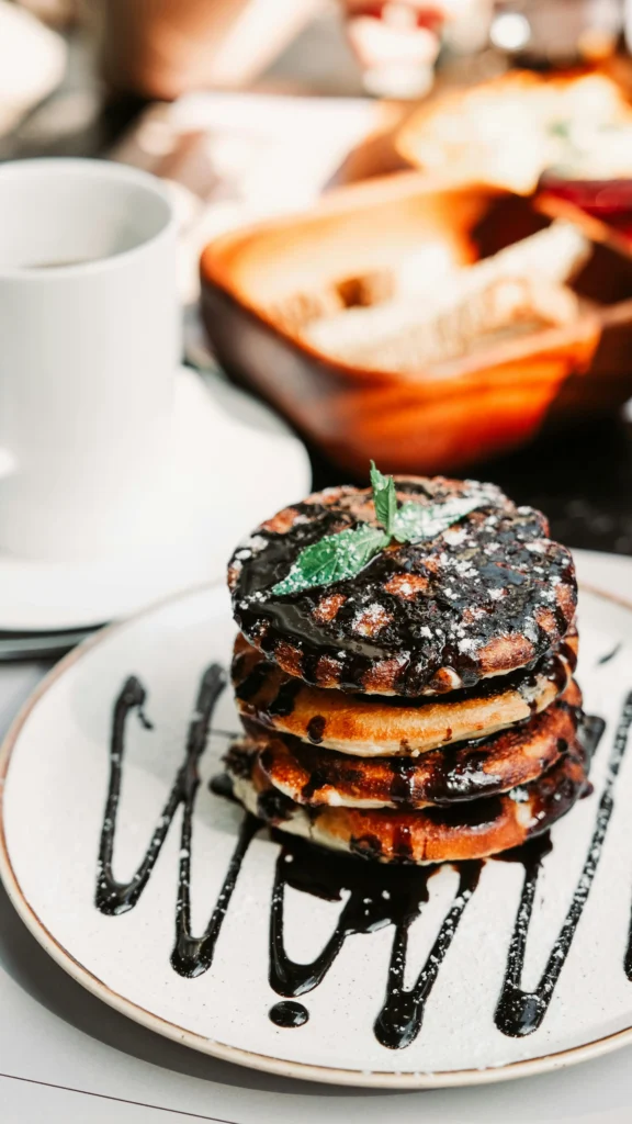 A stack of chocolate chip pancakes drizzled with chocolate syrup