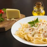 Homemade Alfredo pasta with a wedge of Parmesan, fresh basil, and cherry tomatoes on the side