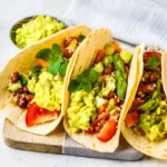 Three vibrant vegetarian burritos filled with fresh vegetables, guacamole, and garnished with basil leaves, served on a wooden board.